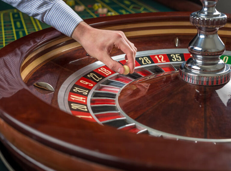 La main d'une personne place une bille sur une roulette qui tourne, à une table de casino.